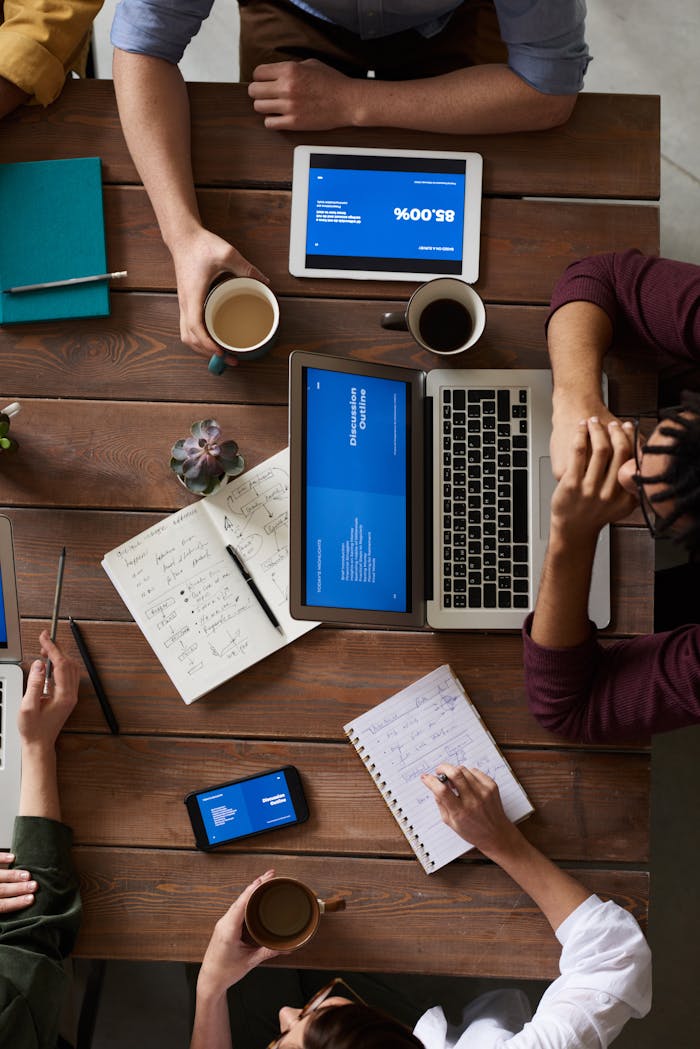 About Group of coworkers discussing business strategies with laptops and tablets in a modern office setting.